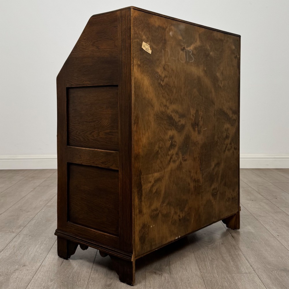 A dark oak slant-front writing bureau featuring carved linenfold upper panels, a single carved drawer with wooden knobs, and a double-door cupboard base decorated with diamond lozenge carvings. View V