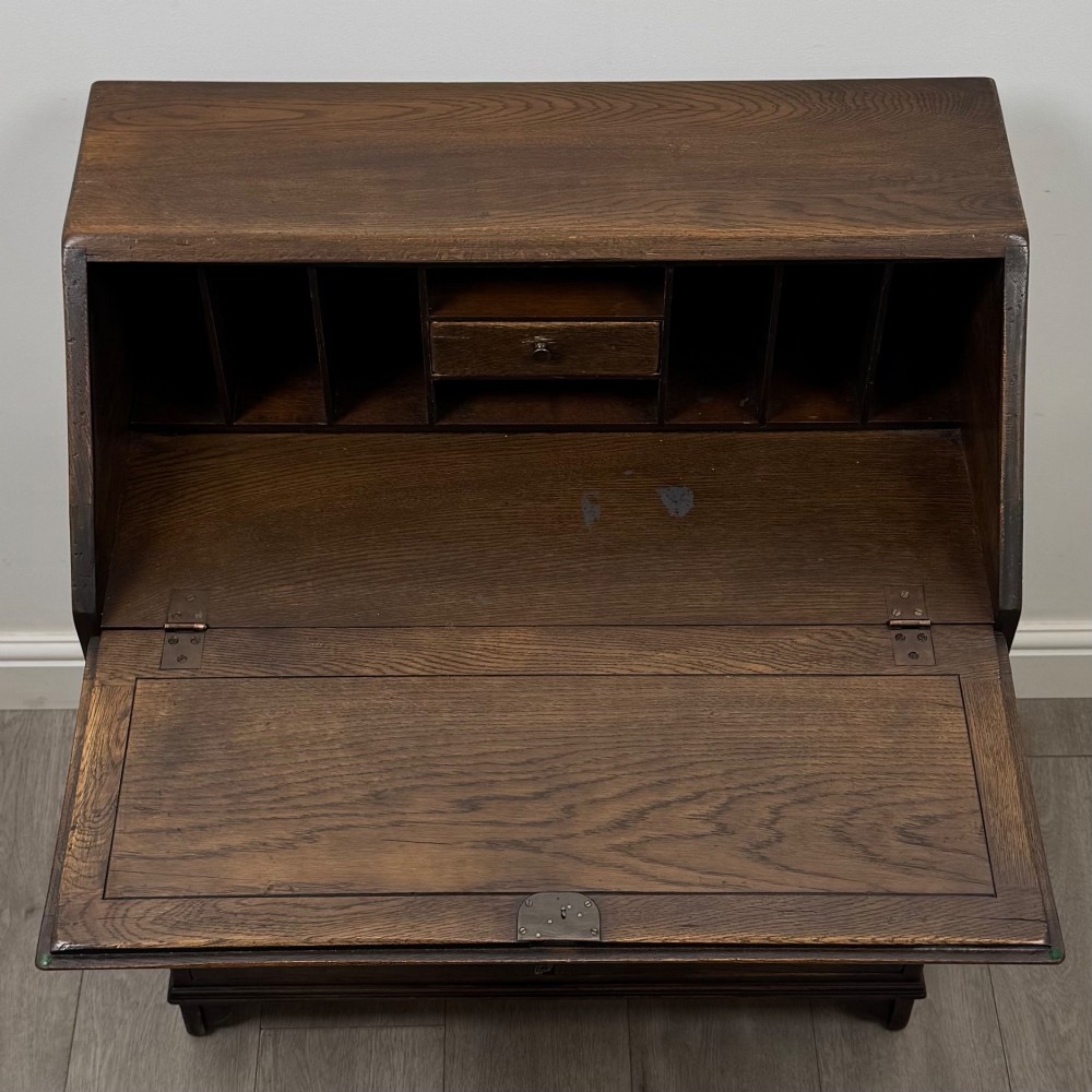 A dark oak slant-front writing bureau featuring carved linenfold upper panels, a single carved drawer with wooden knobs, and a double-door cupboard base decorated with diamond lozenge carvings. View XI