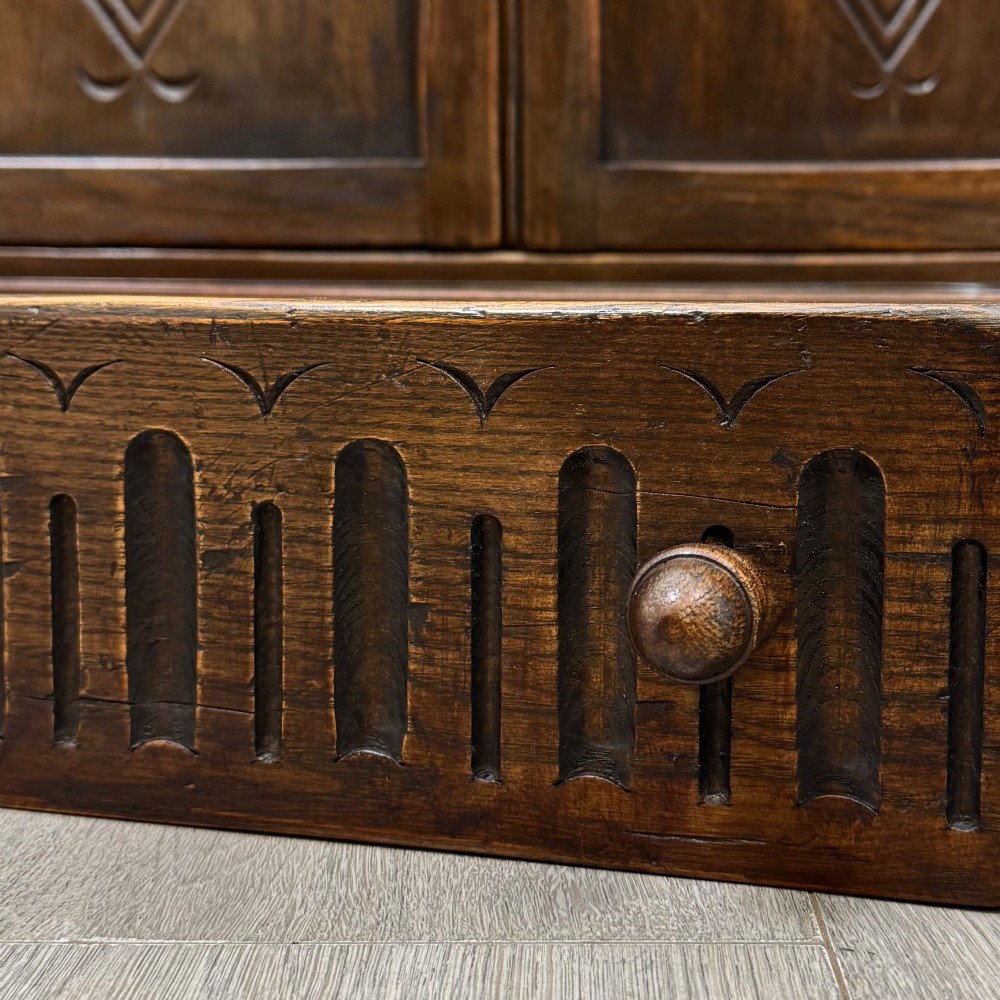 A dark oak slant-front writing bureau featuring carved linenfold upper panels, a single carved drawer with wooden knobs, and a double-door cupboard base decorated with diamond lozenge carvings. View XIII