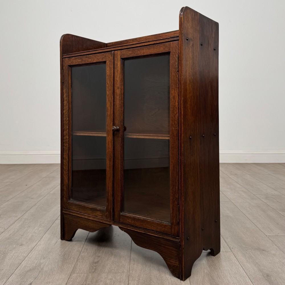 An early 20th-century dark oak display cabinet featuring twin glazed doors, an interior shelf, and a gallery top. View III