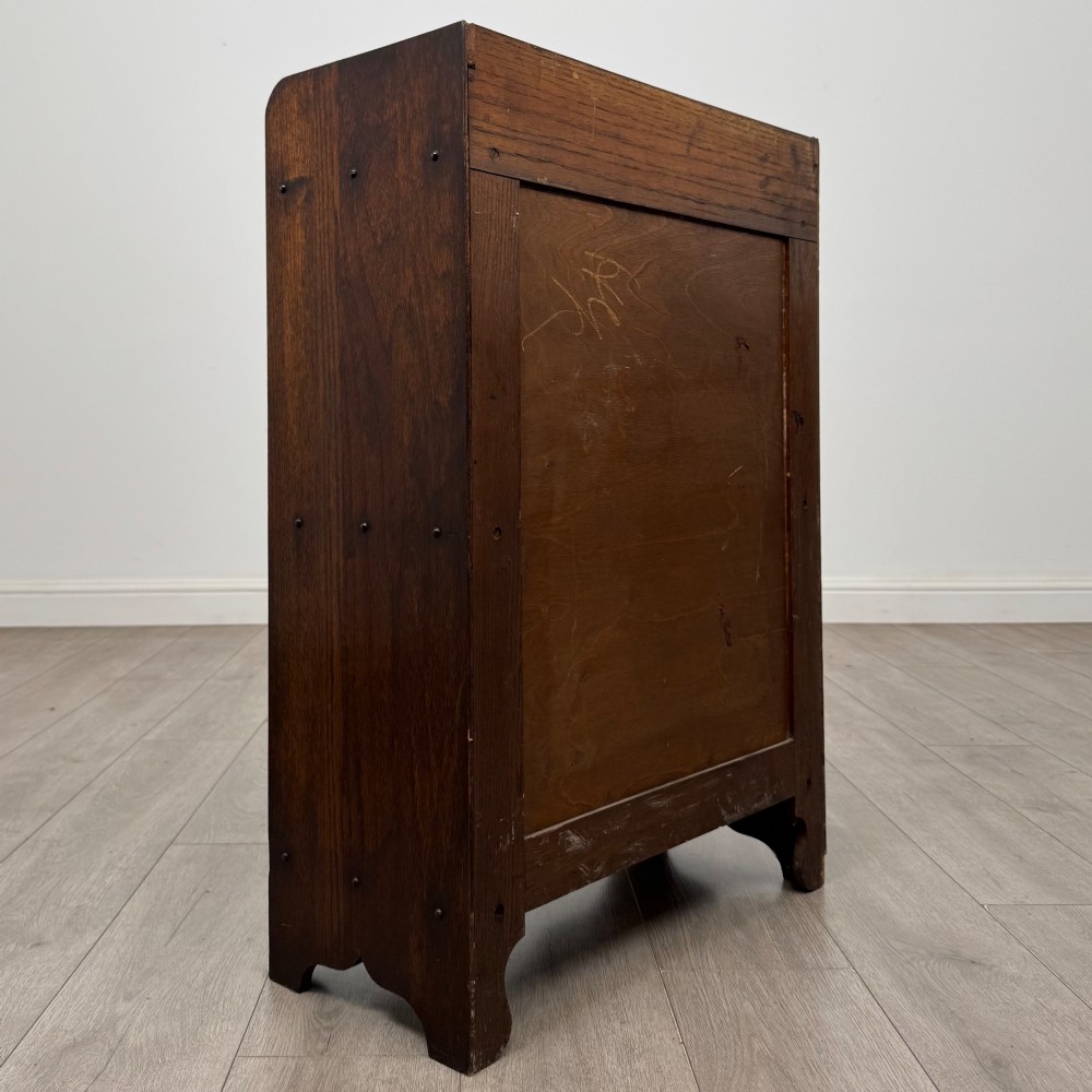 An early 20th-century dark oak display cabinet featuring twin glazed doors, an interior shelf, and a gallery top. View V