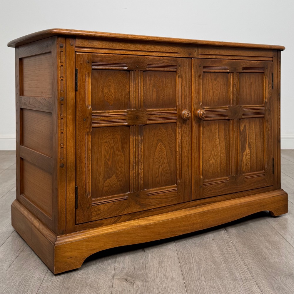 A two-door golden oak storage cupboard featuring geometric panelled doors, turned timber knobs, and a low plinth base. View IX