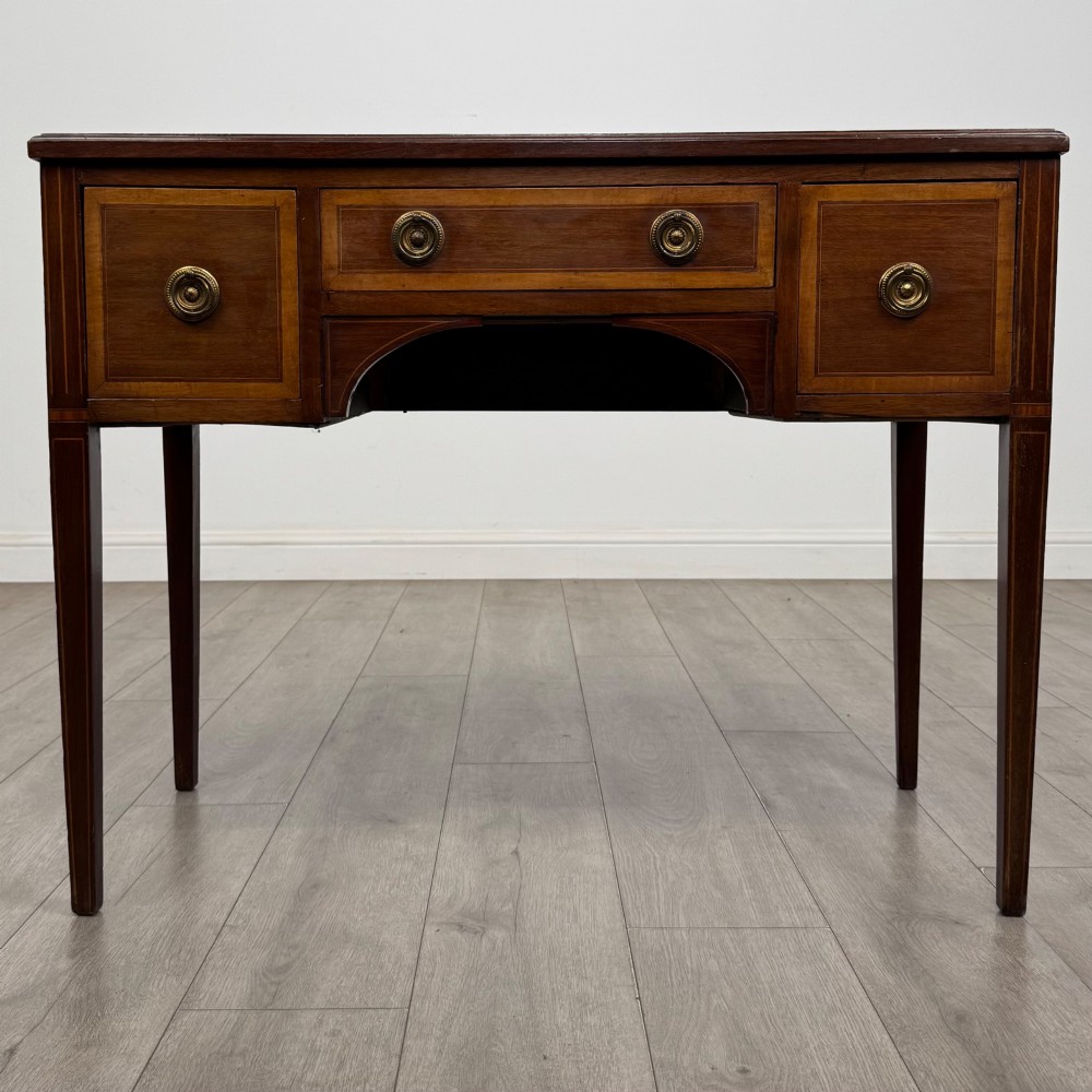 An Edwardian mahogany writing table featuring three drawers with satinwood crossbanding, brass ring pull handles, and square tapered legs.