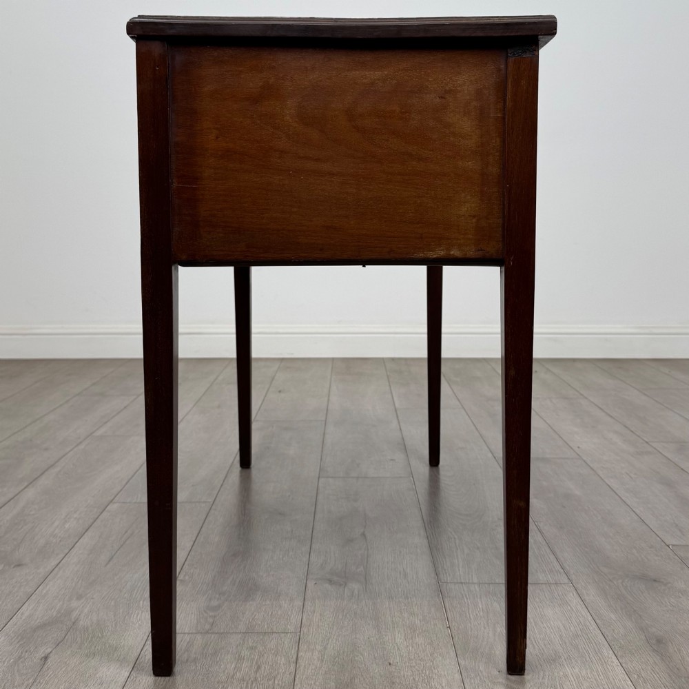 An Edwardian mahogany writing table featuring three drawers with satinwood crossbanding, brass ring pull handles, and square tapered legs. View III