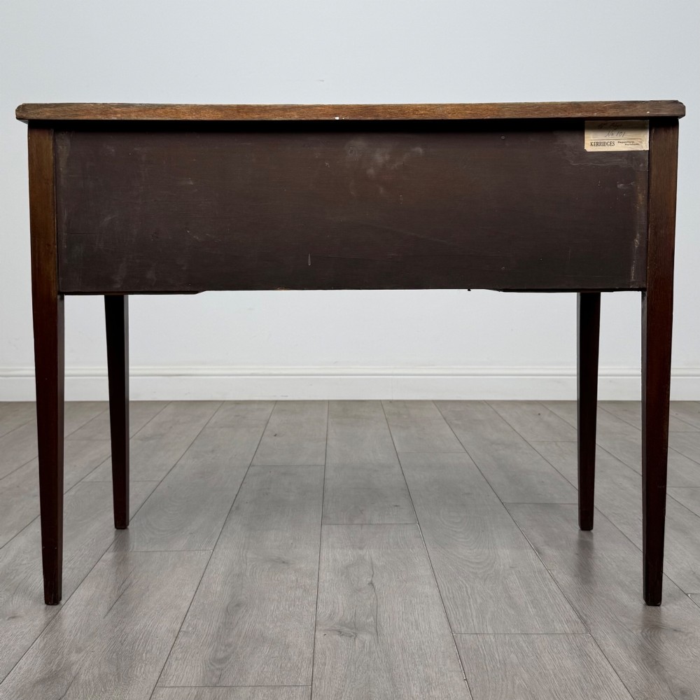 An Edwardian mahogany writing table featuring three drawers with satinwood crossbanding, brass ring pull handles, and square tapered legs. View V