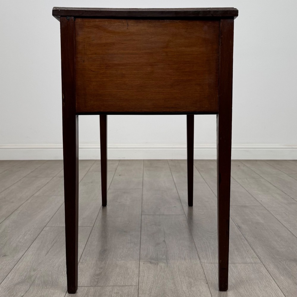 An Edwardian mahogany writing table featuring three drawers with satinwood crossbanding, brass ring pull handles, and square tapered legs. View VII