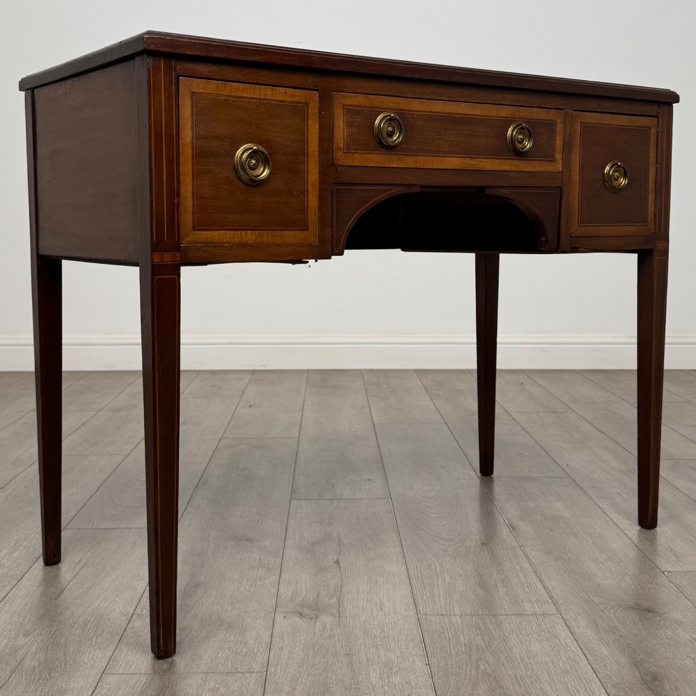 An Edwardian mahogany writing table featuring three drawers with satinwood crossbanding, brass ring pull handles, and square tapered legs. View VIII