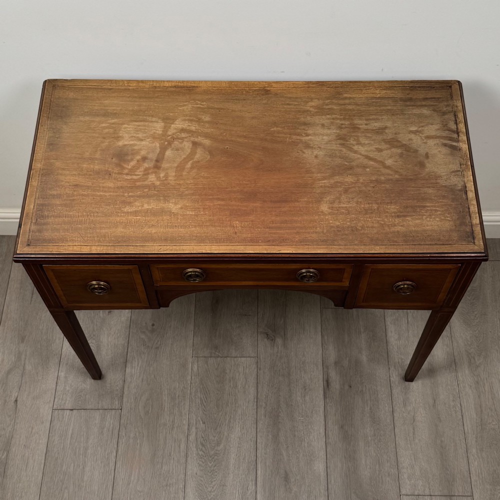 An Edwardian mahogany writing table featuring three drawers with satinwood crossbanding, brass ring pull handles, and square tapered legs. View IX
