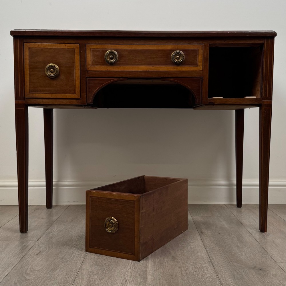 An Edwardian mahogany writing table featuring three drawers with satinwood crossbanding, brass ring pull handles, and square tapered legs. View X