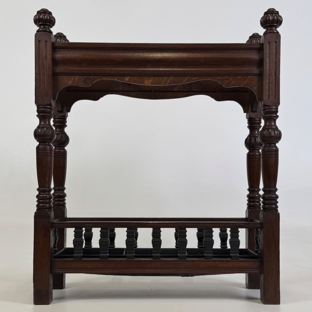 An Edwardian dark oak umbrella stand featuring four turned corner posts topped with finials, a shaped upper crossbar, and a lower spindle gallery enclosing a drip tray.