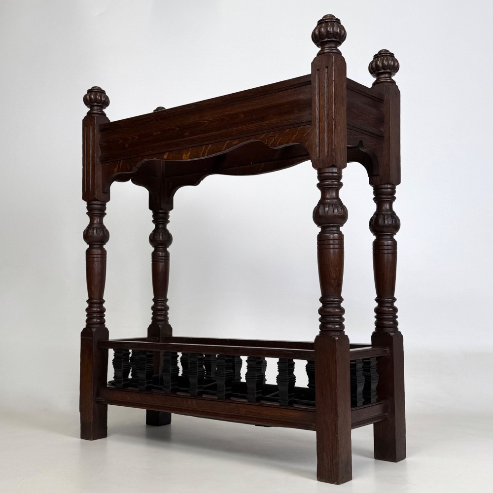 An Edwardian dark oak umbrella stand featuring four turned corner posts topped with finials, a shaped upper crossbar, and a lower spindle gallery enclosing a drip tray. View II