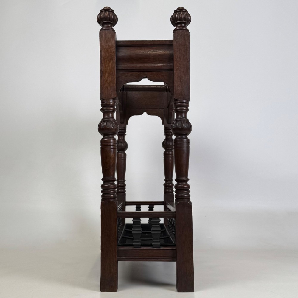 An Edwardian dark oak umbrella stand featuring four turned corner posts topped with finials, a shaped upper crossbar, and a lower spindle gallery enclosing a drip tray. View III