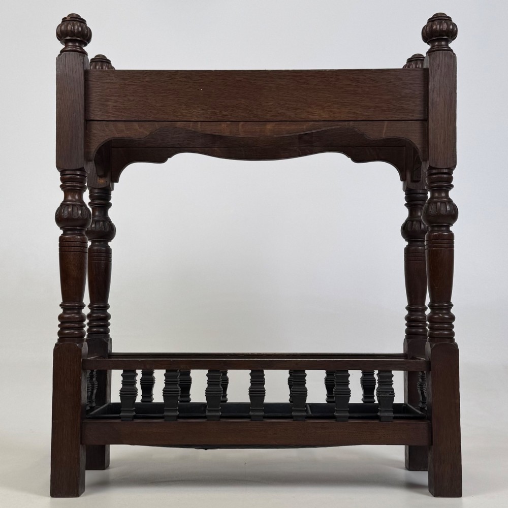 An Edwardian dark oak umbrella stand featuring four turned corner posts topped with finials, a shaped upper crossbar, and a lower spindle gallery enclosing a drip tray. View V
