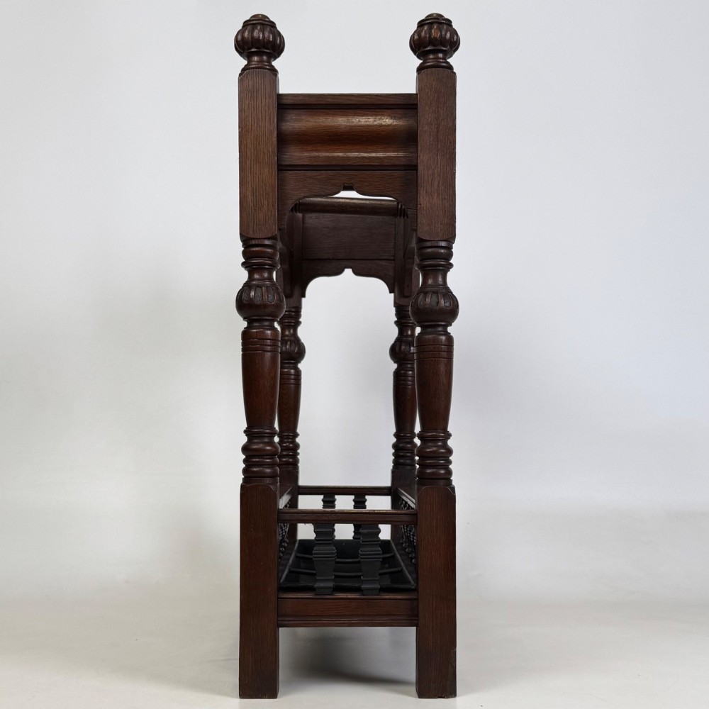 An Edwardian dark oak umbrella stand featuring four turned corner posts topped with finials, a shaped upper crossbar, and a lower spindle gallery enclosing a drip tray. View VII