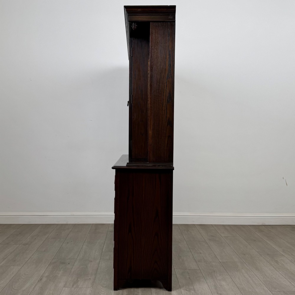 A dark oak display cabinet with a leaded glass central upper cupboard, flanked by open shelves, set atop a lower unit with multiple drawers and carved cupboard doors. View V