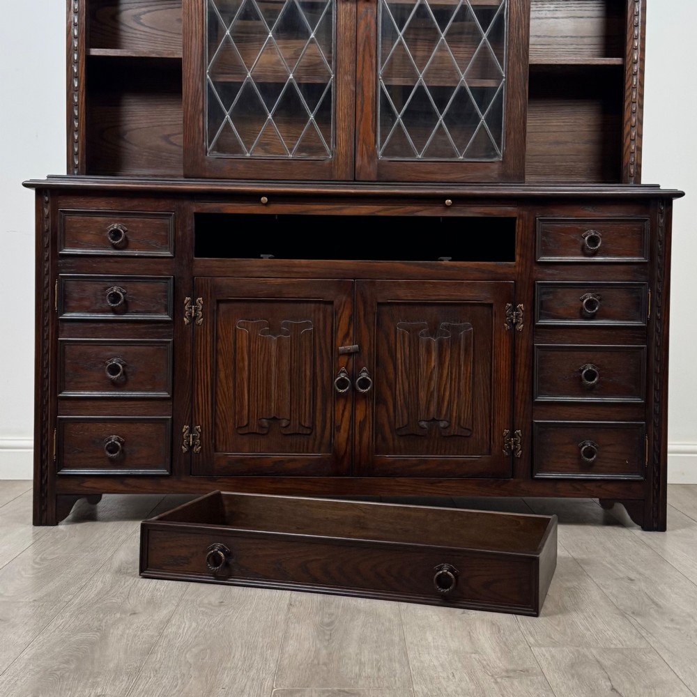 A dark oak display cabinet with a leaded glass central upper cupboard, flanked by open shelves, set atop a lower unit with multiple drawers and carved cupboard doors. View XII