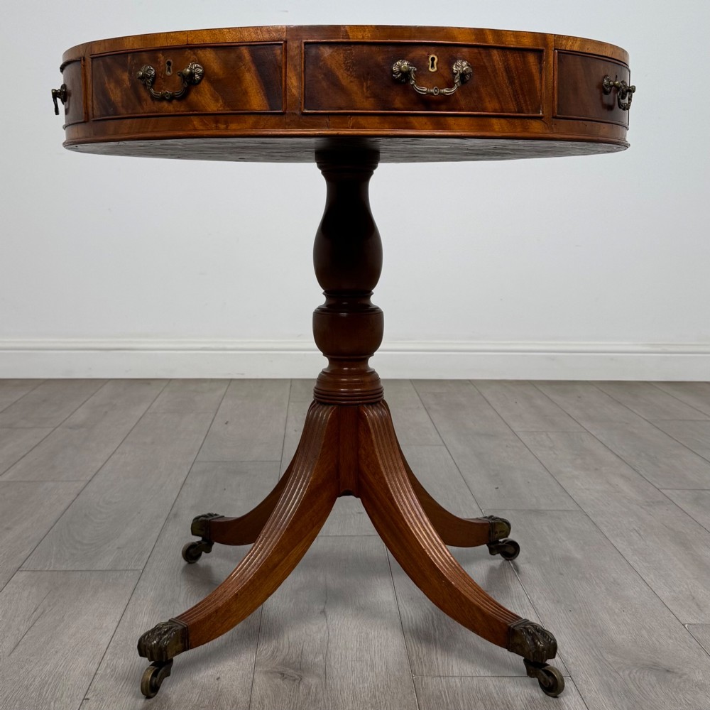 A small Regency style circular mahogany drum table featuring frieze drawers with brass handles, supported by a central turned pedestal and reeded splayed legs on brass castors.
