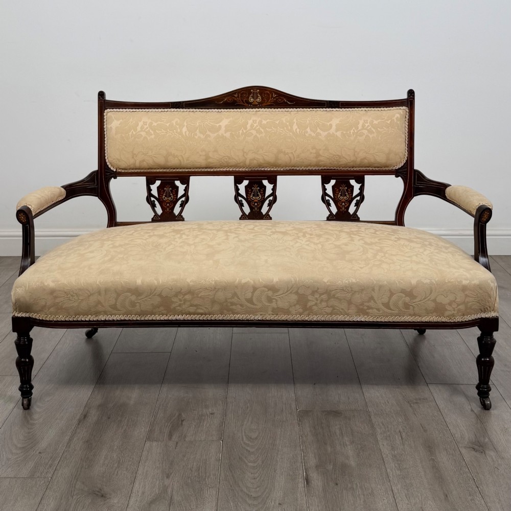 An antique Victorian rosewood settee featuring central backrest marquetry inlay, open armrests, turned front legs on castors, and cream damask upholstery.