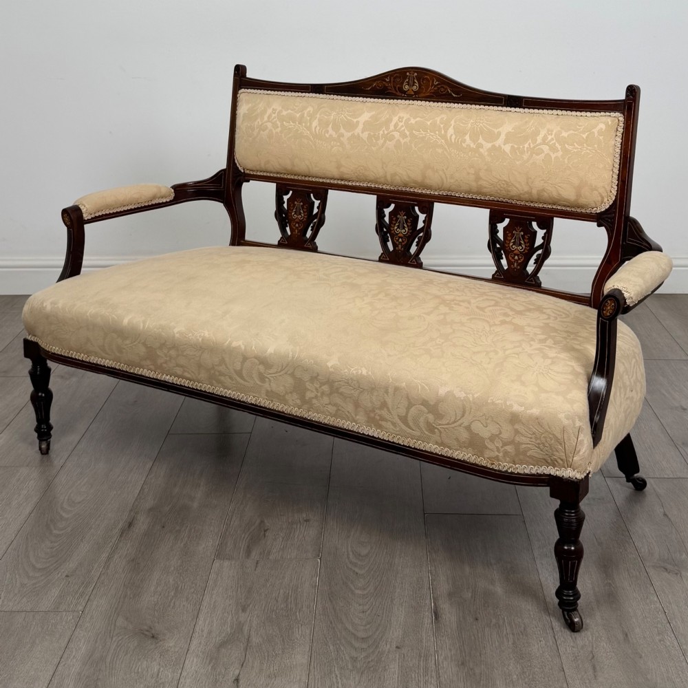 An antique Victorian rosewood settee featuring central backrest marquetry inlay, open armrests, turned front legs on castors, and cream damask upholstery. View II