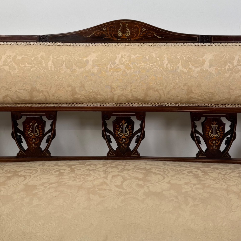 An antique Victorian rosewood settee featuring central backrest marquetry inlay, open armrests, turned front legs on castors, and cream damask upholstery. View XI