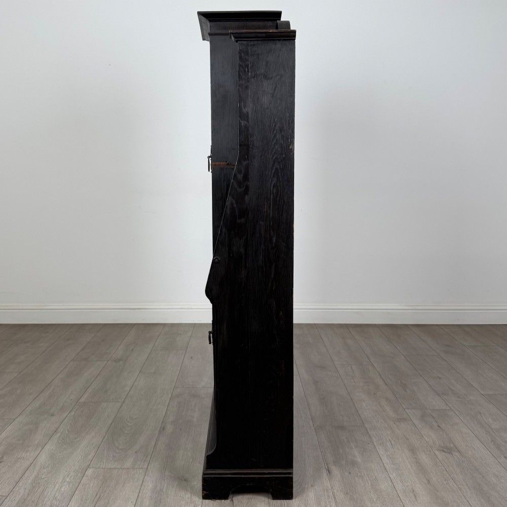 An ebonised oak bureau bookcase featuring an asymmetrical design with a glazed door cabinet, a slanted fall-front writing surface, open shelving, and a heart cutout crest. View V