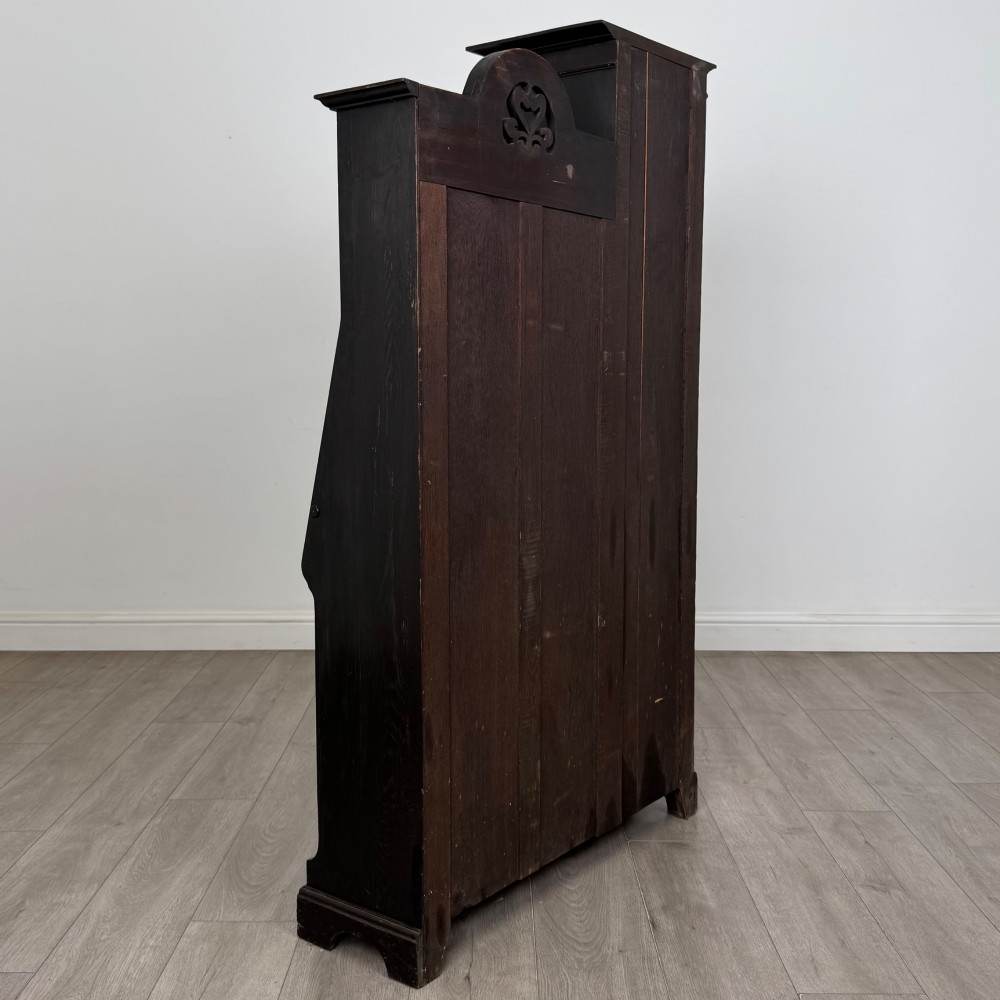 An ebonised oak bureau bookcase featuring an asymmetrical design with a glazed door cabinet, a slanted fall-front writing surface, open shelving, and a heart cutout crest. View VI