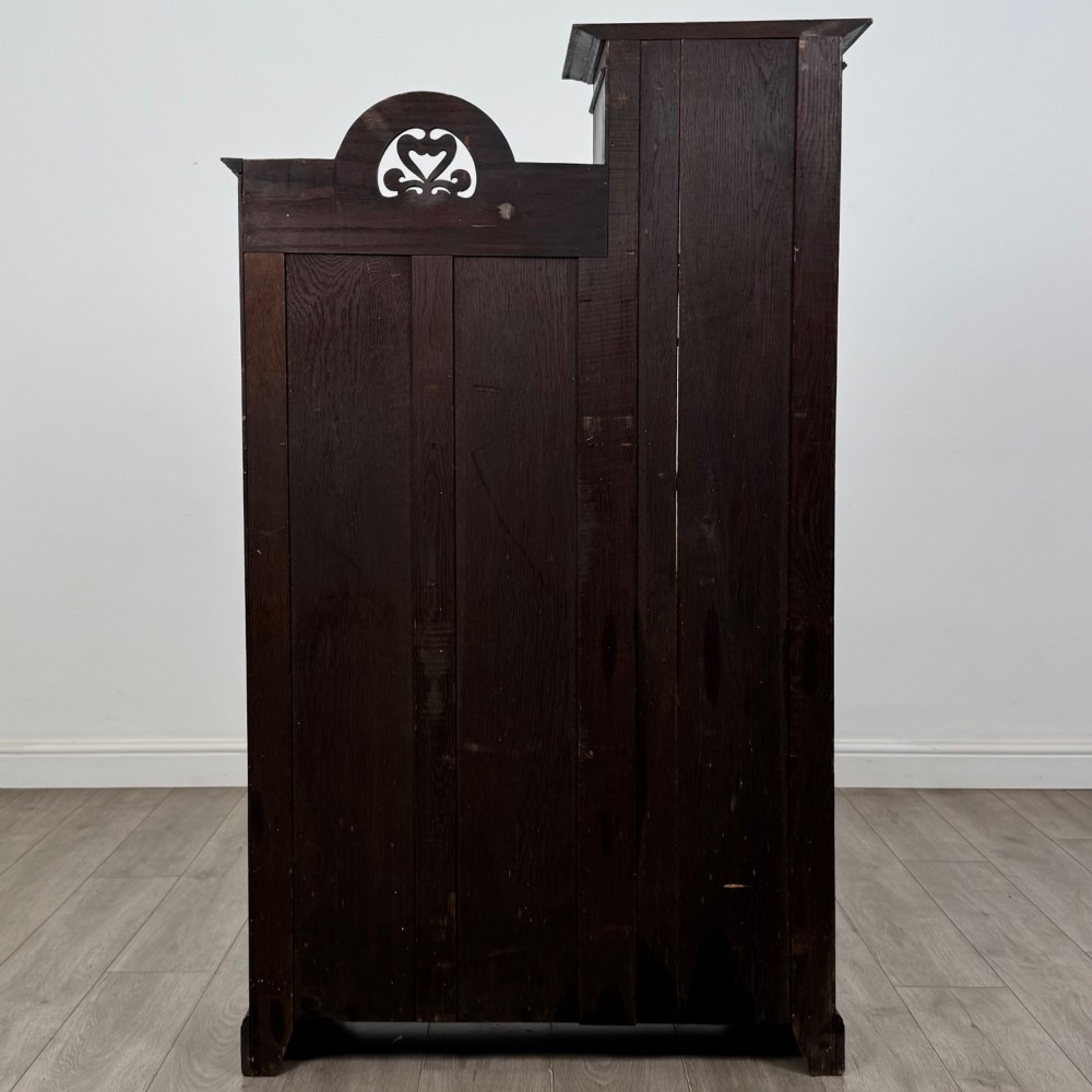 An ebonised oak bureau bookcase featuring an asymmetrical design with a glazed door cabinet, a slanted fall-front writing surface, open shelving, and a heart cutout crest. View VII