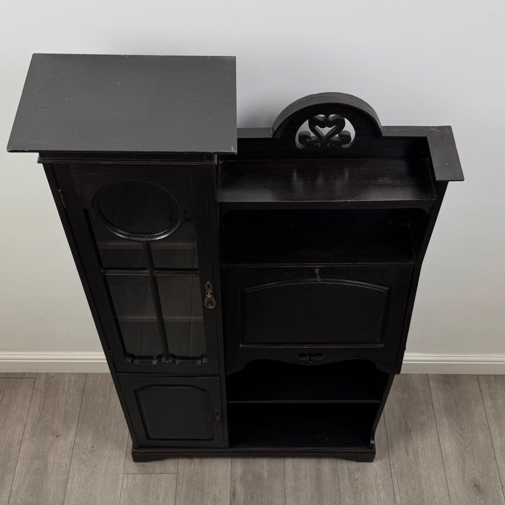 An ebonised oak bureau bookcase featuring an asymmetrical design with a glazed door cabinet, a slanted fall-front writing surface, open shelving, and a heart cutout crest. View XI