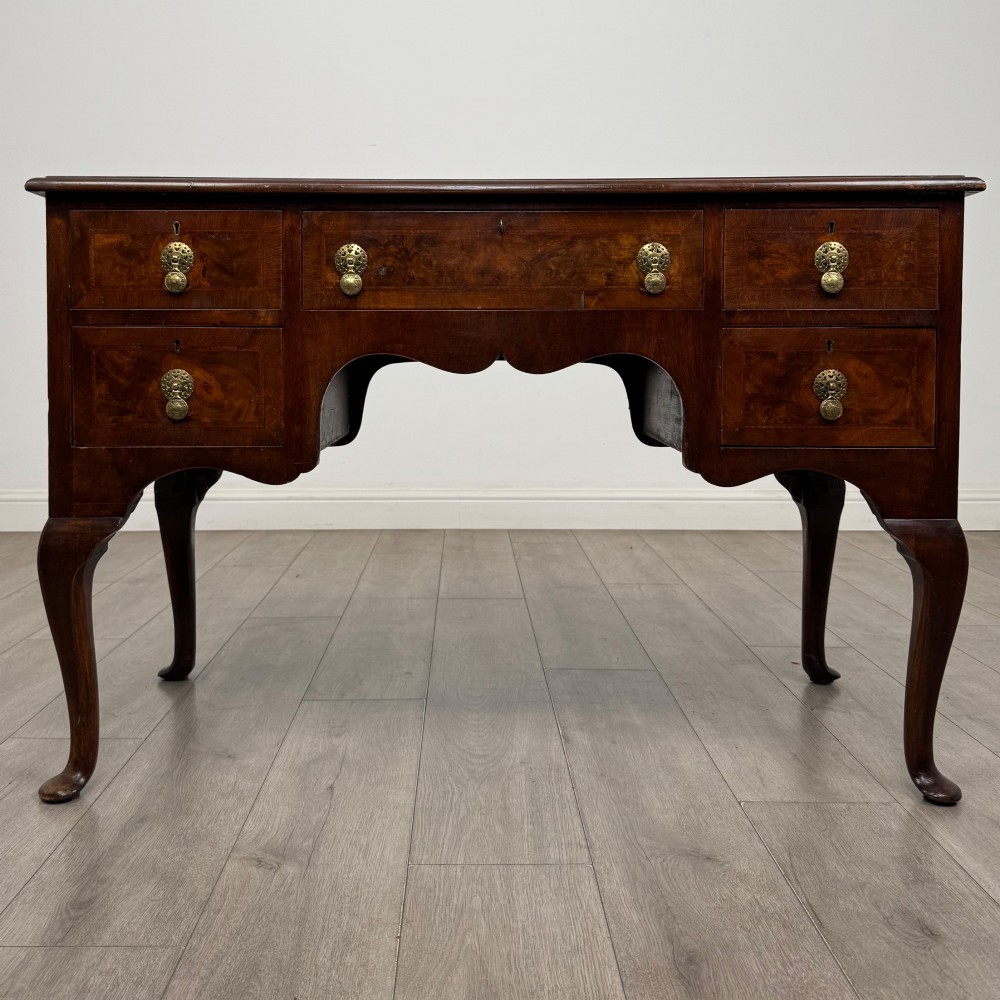 A 19th-century Victorian writing table crafted from burr walnut with five drawer fronts, ornate brass drop handles, a shaped central kneehole, and cabriole legs.