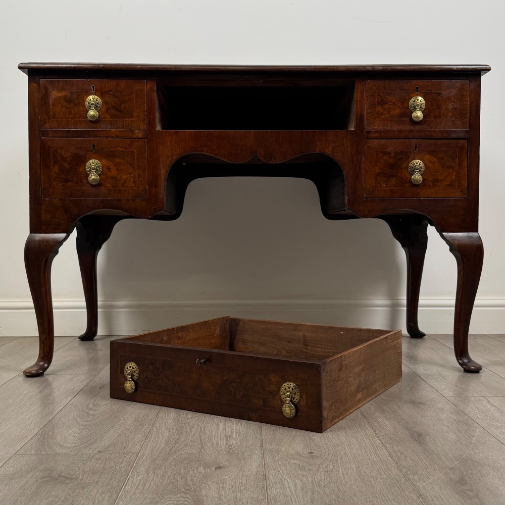 A 19th-century Victorian writing table crafted from burr walnut with five drawer fronts, ornate brass drop handles, a shaped central kneehole, and cabriole legs. View X