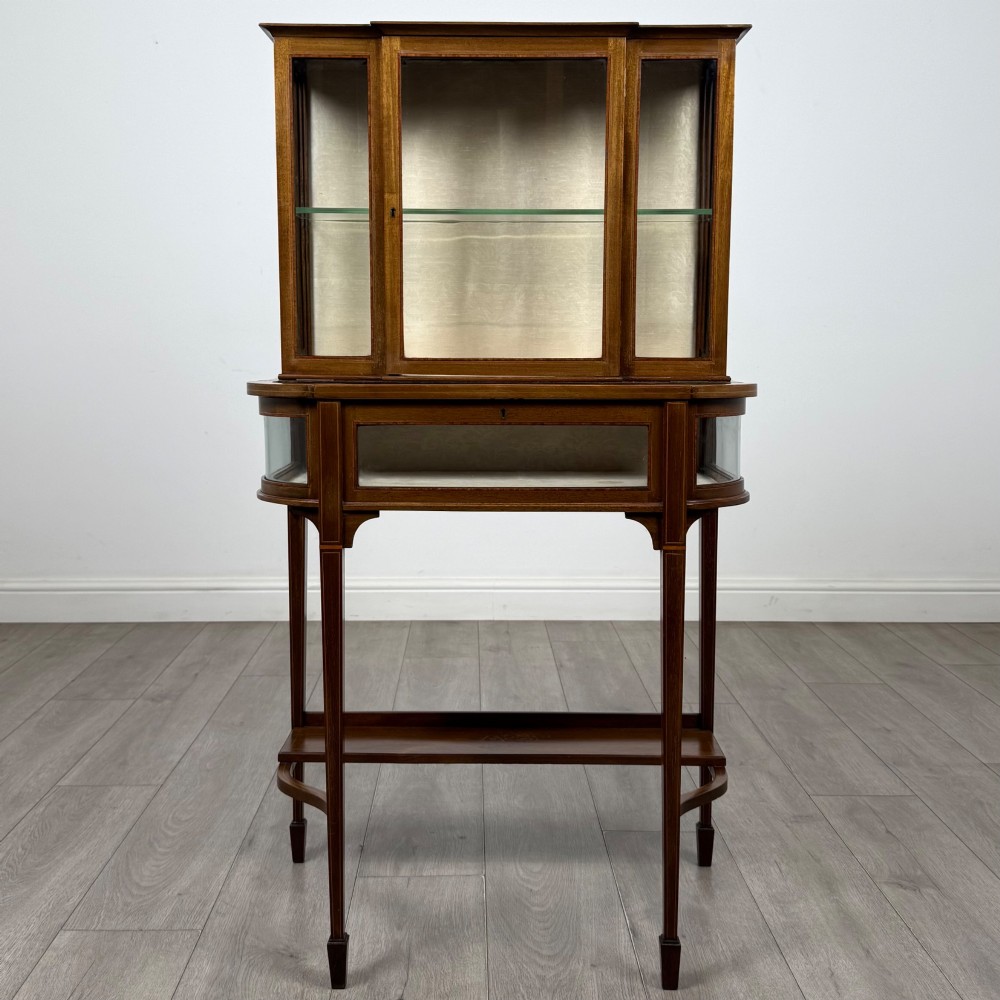 An Edwardian mahogany glazed display cabinet featuring tapered legs, line inlay detailing, glass shelves, and a lower undertier shelf.