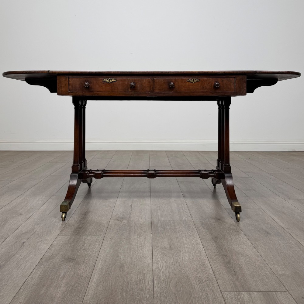 A 19th-century Regency style yew wood side table featuring drop-leaf ends, twin drawers with brass escutcheons and round knobs, turned twin-stem supports, a stretcher, and brass castors. View II