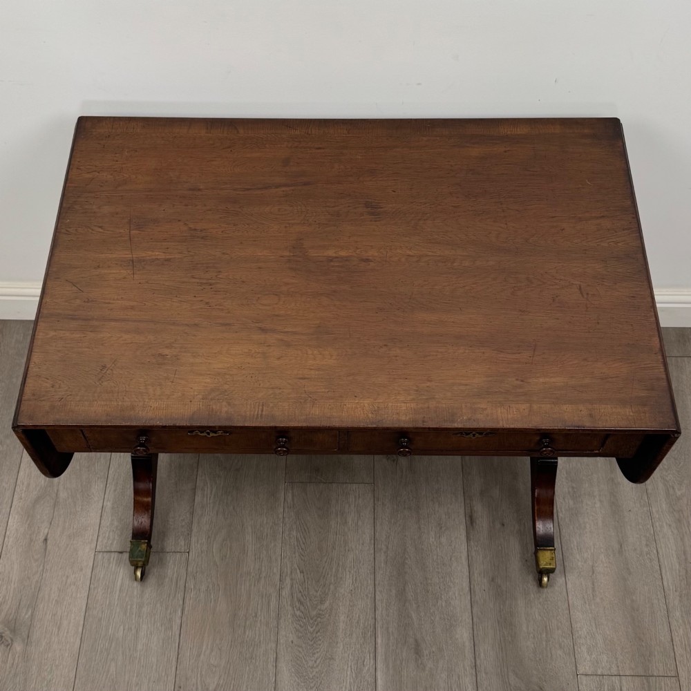 A 19th-century Regency style yew wood side table featuring drop-leaf ends, twin drawers with brass escutcheons and round knobs, turned twin-stem supports, a stretcher, and brass castors. View X