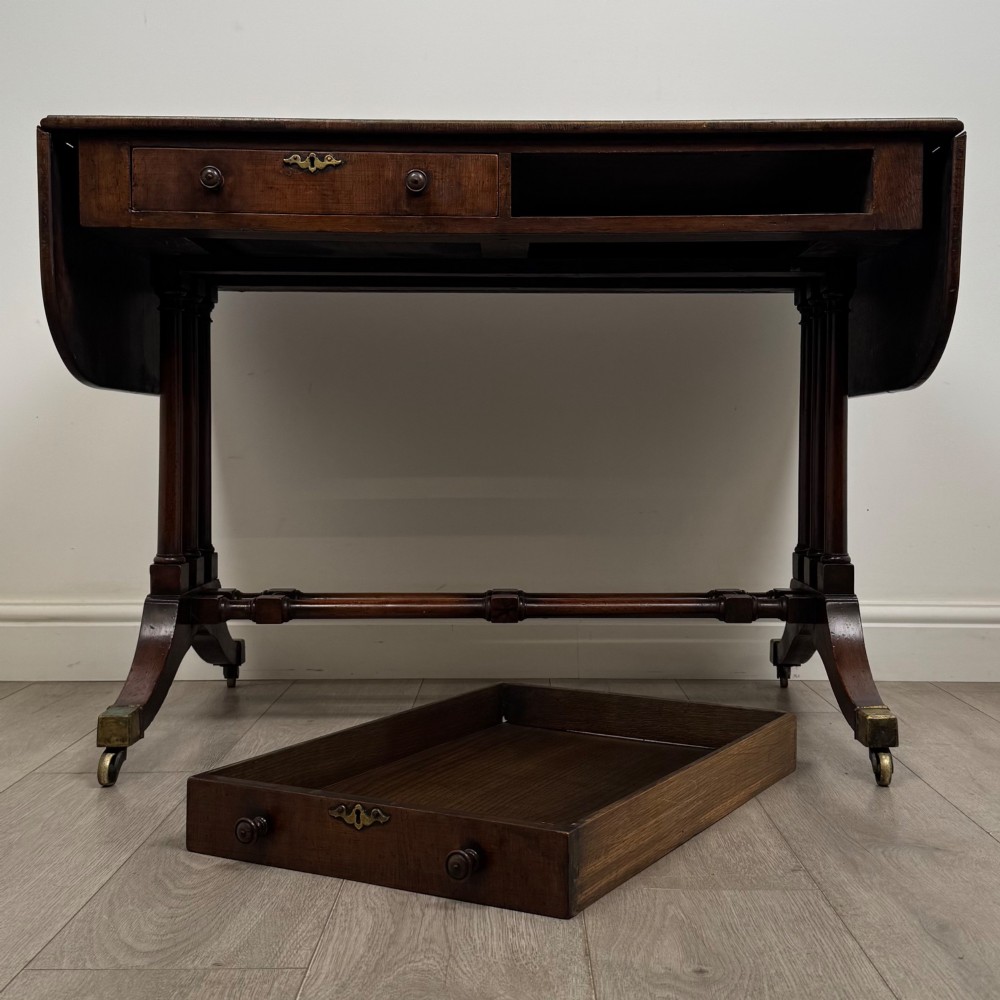 A 19th-century Regency style yew wood side table featuring drop-leaf ends, twin drawers with brass escutcheons and round knobs, turned twin-stem supports, a stretcher, and brass castors. View XII