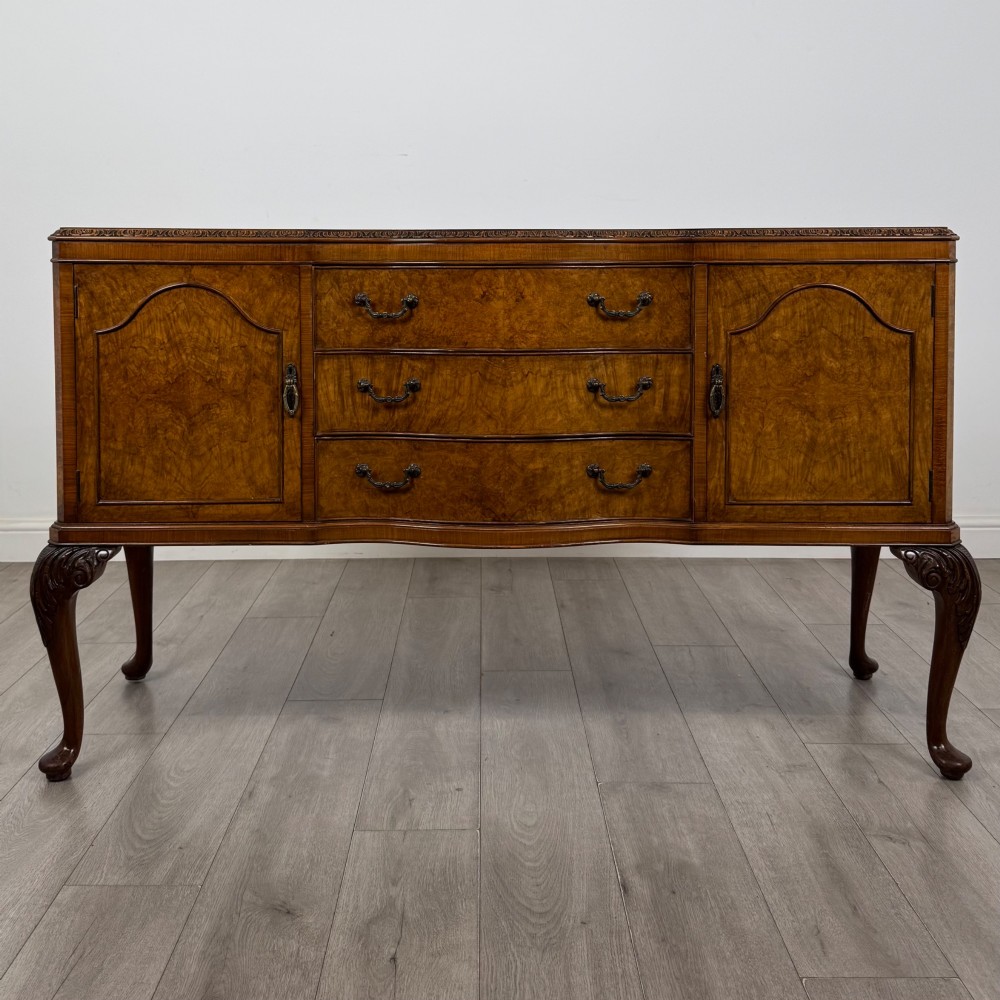 An Edwardian burr walnut sideboard featuring three central drawers flanked by two cupboard doors, set on carved cabriole legs.