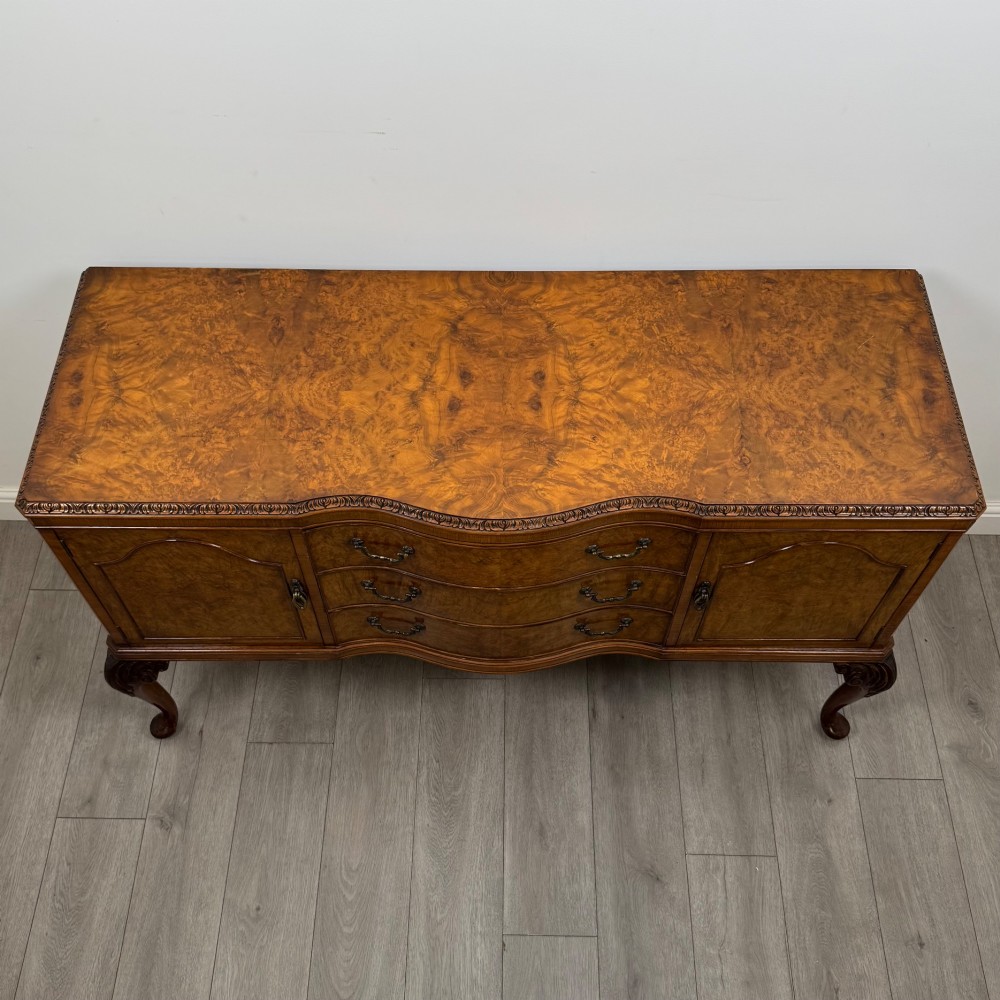 An Edwardian burr walnut sideboard featuring three central drawers flanked by two cupboard doors, set on carved cabriole legs. View X