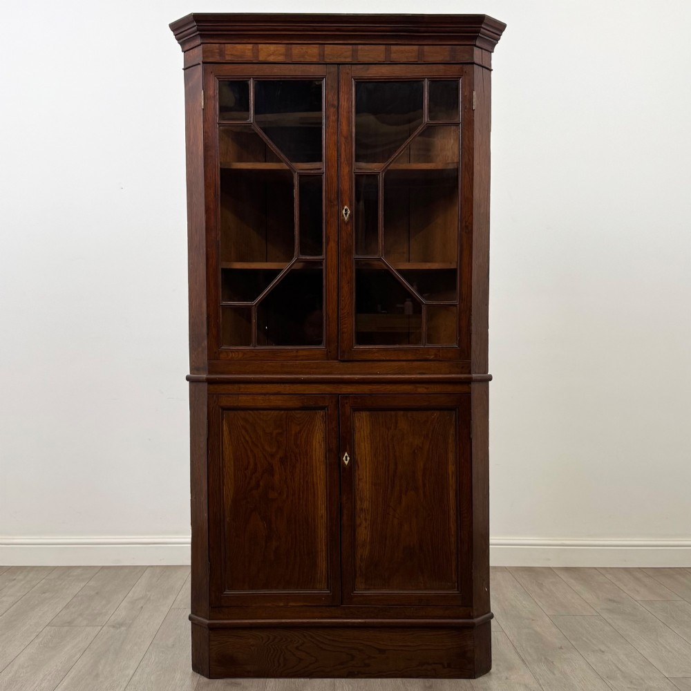 An eighteenth century Georgian dark oak standing corner cabinet featuring upper geometric astragal glazed doors and lower panelled cupboard doors.