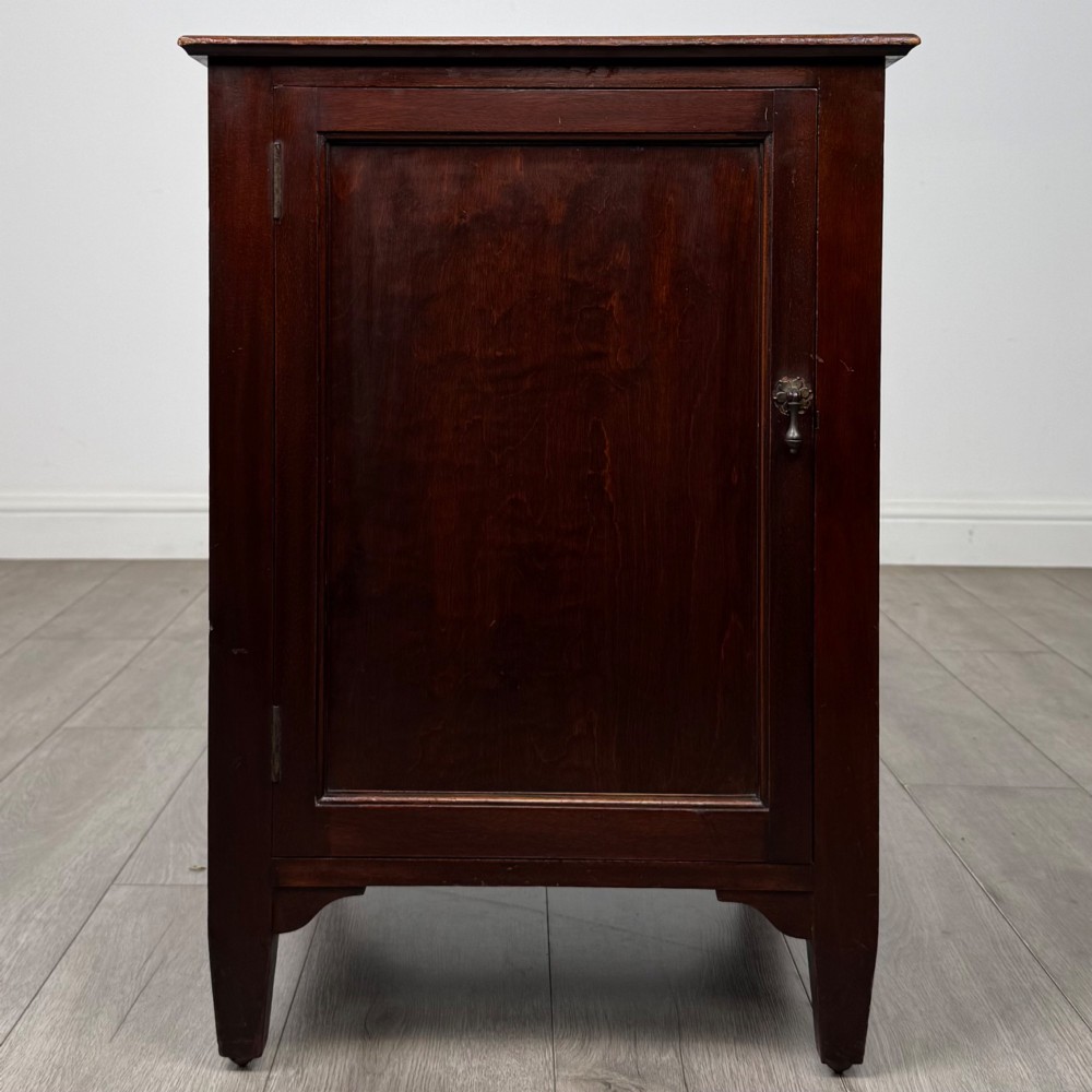A dark stained oak Edwardian cupboard featuring a single panel door, teardrop handle, and square tapered legs.