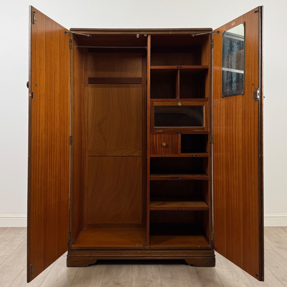 A freestanding mid-20th-century double wardrobe crafted from medium brown oak with twin flush doors, small circular wooden handles, and a low plinth base. View II