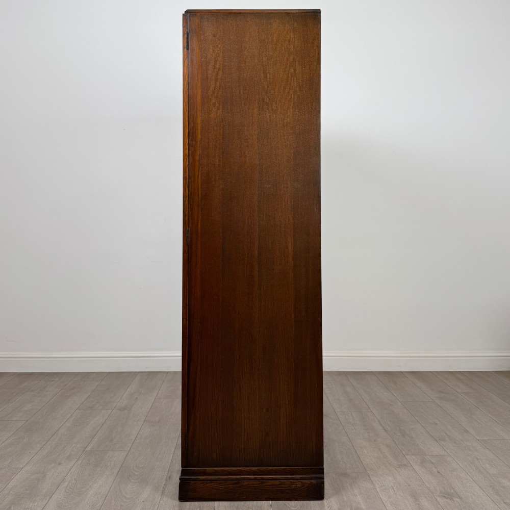A freestanding mid-20th-century double wardrobe crafted from medium brown oak with twin flush doors, small circular wooden handles, and a low plinth base. View IV