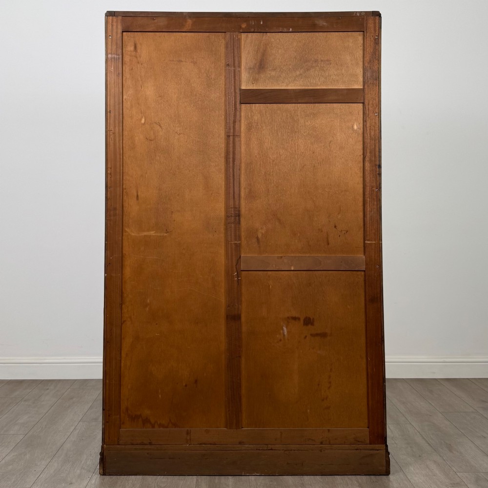 A freestanding mid-20th-century double wardrobe crafted from medium brown oak with twin flush doors, small circular wooden handles, and a low plinth base. View VI