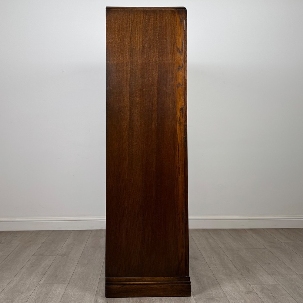 A freestanding mid-20th-century double wardrobe crafted from medium brown oak with twin flush doors, small circular wooden handles, and a low plinth base. View VIII