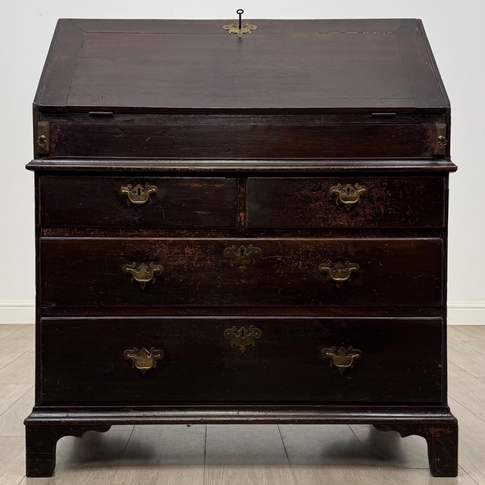 An 18th-century dark oak Georgian bureau with a slant-front writing slope, brass batwing drop handles, and bracket feet.