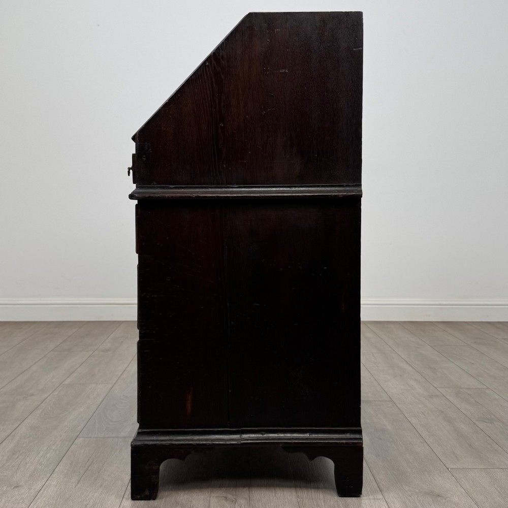 An 18th-century dark oak Georgian bureau with a slant-front writing slope, brass batwing drop handles, and bracket feet. View IV