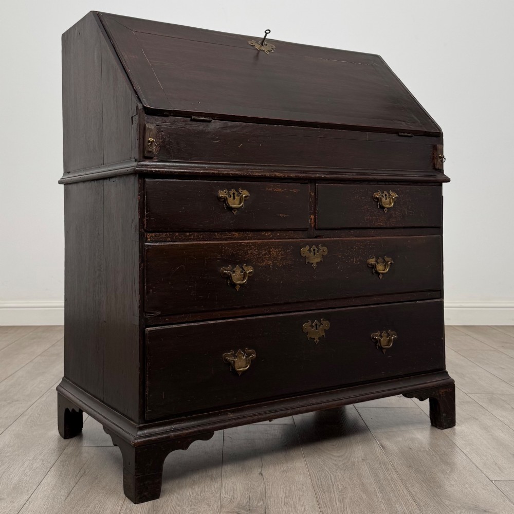 An 18th-century dark oak Georgian bureau with a slant-front writing slope, brass batwing drop handles, and bracket feet. View IX