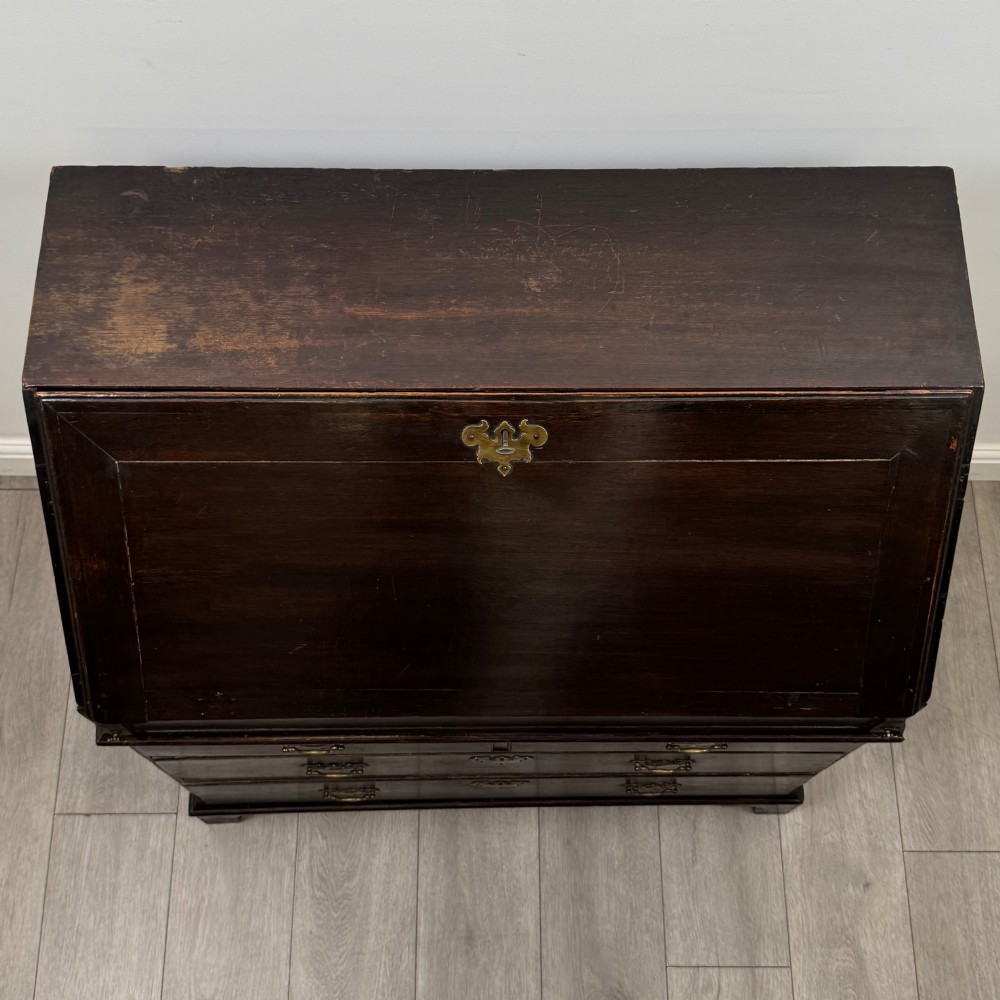 An 18th-century dark oak Georgian bureau with a slant-front writing slope, brass batwing drop handles, and bracket feet. View X