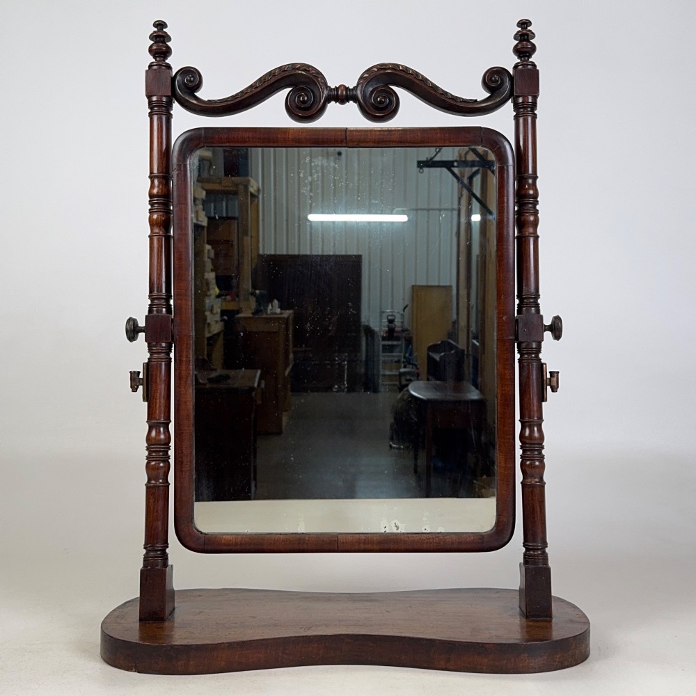 A 19th-century mahogany dressing mirror with turned side columns, carved scrollwork cresting, and an adjustable rectangular glass frame on a shaped base. View II