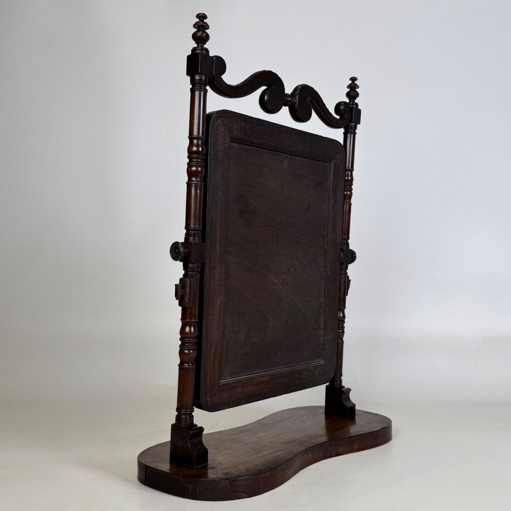 A 19th-century mahogany dressing mirror with turned side columns, carved scrollwork cresting, and an adjustable rectangular glass frame on a shaped base. View VI