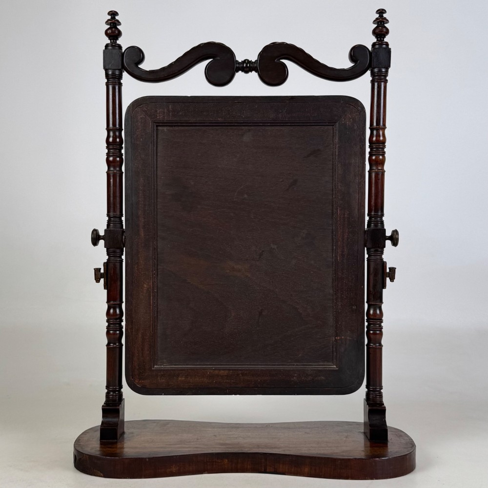 A 19th-century mahogany dressing mirror with turned side columns, carved scrollwork cresting, and an adjustable rectangular glass frame on a shaped base. View VII