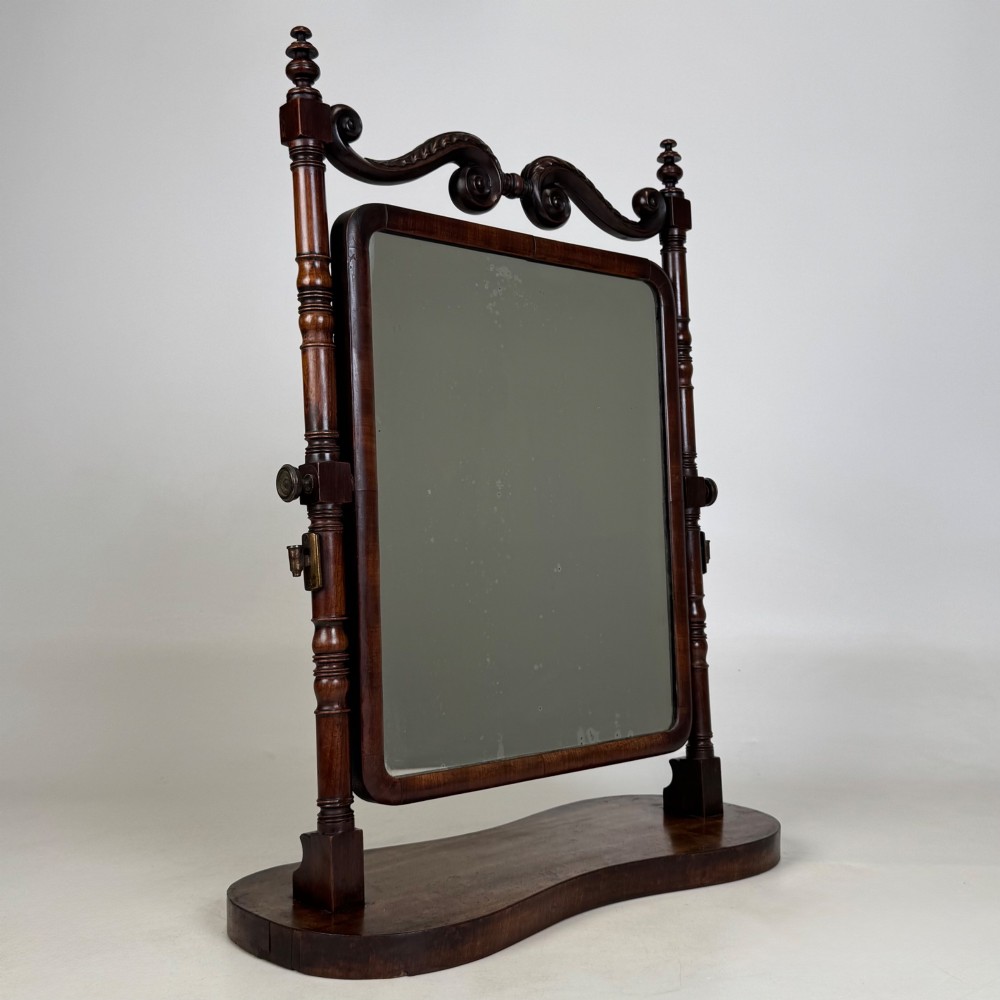 A 19th-century mahogany dressing mirror with turned side columns, carved scrollwork cresting, and an adjustable rectangular glass frame on a shaped base. View X